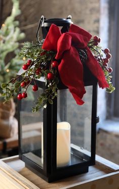 a lantern with a red bow on it and a candle in front of a christmas tree