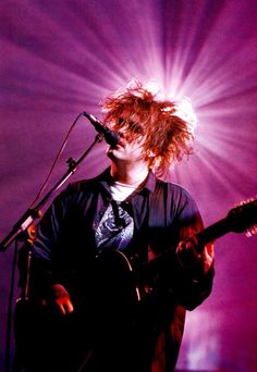 a man with red hair playing an acoustic guitar in front of a microphone on stage