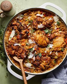 a large pot filled with chicken and rice next to a wooden spoon on top of a table