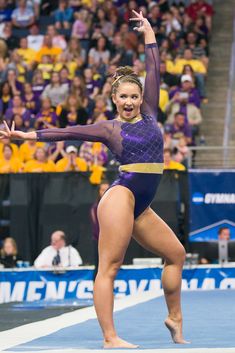 a woman in a purple leotard doing a trick on the balance beam at a competition