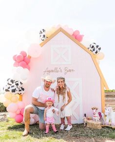 a man and woman pose with their daughter in front of a barn decorated with balloons