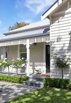 a white house with some flowers on the front porch and bushes in front of it