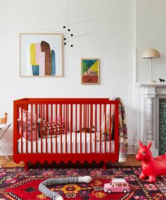 a baby's room with a red crib and toys on the floor in front of it