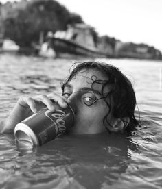 a man is floating in the water drinking from a soda bottle while wearing eye makeup