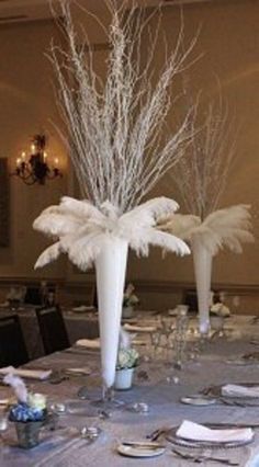 two tall white vases filled with flowers and feathers on top of a dining room table