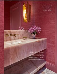 a bathroom with pink walls and marble counter tops, gold faucets and flowers