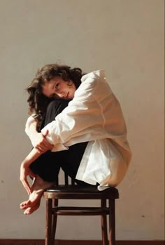 a woman sitting on top of a wooden chair with her arms around the back of her head