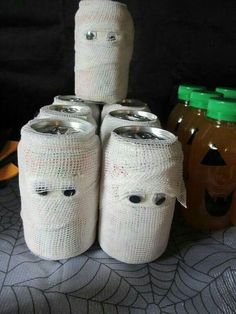 there are four jars wrapped in white paper with faces on them and two pumpkins behind them