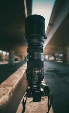 a person holding up a large camera lens in front of a bridge over looking the street