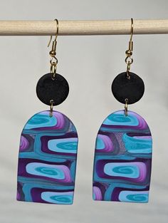 the earrings are hanging from a hook on a wooden hanger with two black circles