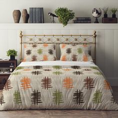 a bed with an orange, green and brown comforter on it in a bedroom