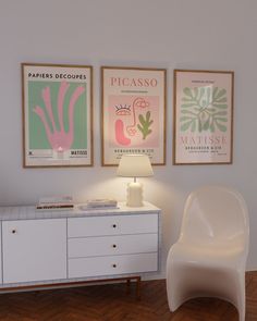 a white chair sitting next to a table with a lamp on top of it in front of two posters