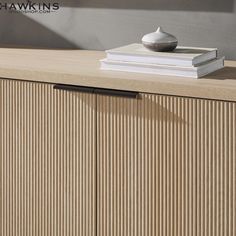 a white vase sitting on top of a wooden cabinet next to a book and magazines