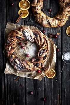 oranges, cranberries and other food are arranged on top of paper with cinnamon sticks