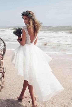 a woman is walking on the beach with flowers in her hand and wearing a white dress