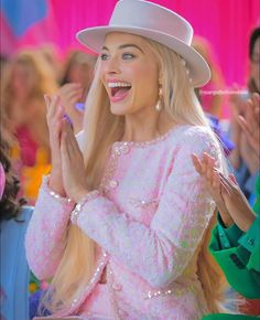 lady with blonde hair wearing a white hat and pink dress clapping in front of a crowd