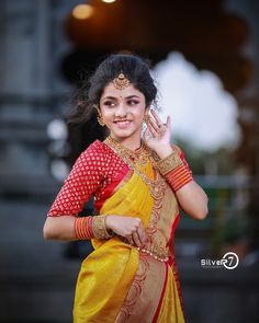 a woman in a yellow and red sari holding her hand up to her ear