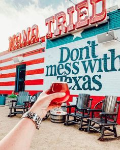 a person holding up a glass of wine in front of a building that says don't mess with texas