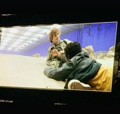 two men are sitting on the ground in front of a screen with an image of them