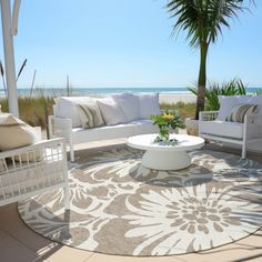 an outdoor living area with white furniture and palm trees on the beach in the background