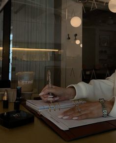 a woman sitting at a desk with her hand on a pen and writing in a notebook