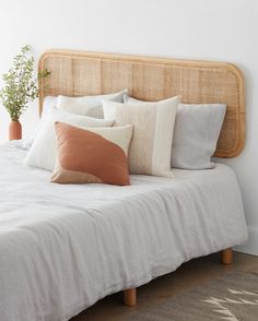 a bed with white sheets and pillows on top of it next to a potted plant