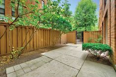 a fenced in area with trees and bushes next to it, surrounded by brick buildings