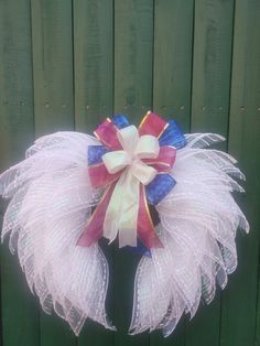 a wreath with white, red and blue feathers hanging on a green wooden fence outside