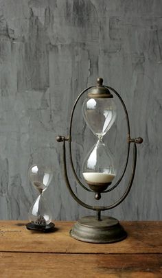 an hourglass sitting on top of a wooden table next to a gray wall with a white candle in it