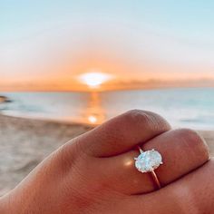 a person's hand holding an engagement ring on the beach