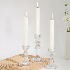 three candles are sitting on a wooden tray next to some glass goblets and flowers