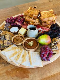 a platter filled with cheese, crackers, fruit and other foods on a wooden table