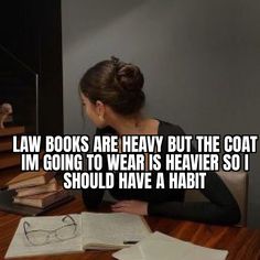 a woman sitting at a desk with books and glasses on it, reading law books are heavy but the coat im going to wear is heaven so i should have a habit