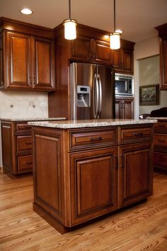 a kitchen with wooden cabinets and stainless steel refrigerator freezer combo in the center, surrounded by hardwood flooring