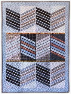 a quilted wall hanging on the side of a white wall with multiple strips of blue and brown