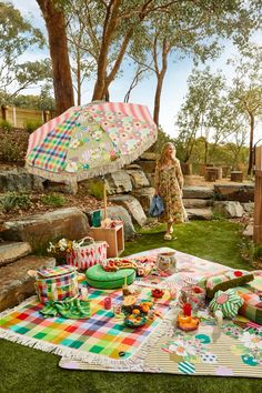 a woman standing next to a picnic table with an umbrella over it and food on the ground