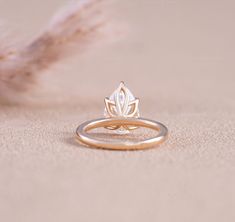 a gold ring with a leaf design on the front and side, sitting next to a feather