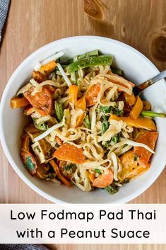 a white bowl filled with noodles and vegetables on top of a wooden table next to a fork