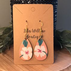 a pair of pink and white flower earrings on top of a wooden table next to a plant