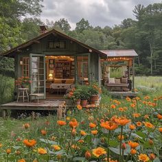 a small cabin in the middle of a field full of flowers and greenery with lights on