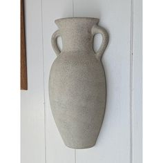 a large gray vase hanging on the side of a white wall next to a wooden door