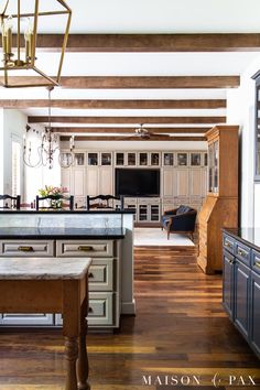 a large kitchen with wooden floors and white cabinets, an island in the middle is surrounded by wood beams