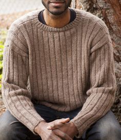 a man sitting in front of a tree wearing a sweater