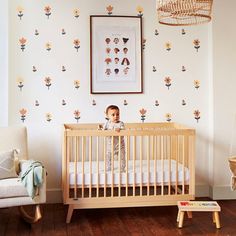 a baby in a crib next to a wall with flowers on it