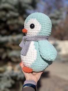 a hand holding a small crocheted penguin with a scarf around it's neck