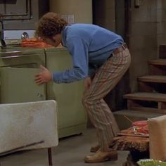 a man leaning over in front of an old fashioned refrigerator and looking at something on the floor