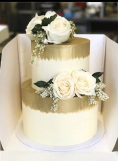 a three tiered cake with white flowers on top and gold stripes around the edges