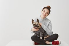 a woman sitting on the floor holding a dog wearing a sweater and leggings