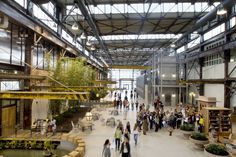 people are walking through an open building with lots of windows and plants on the ceiling