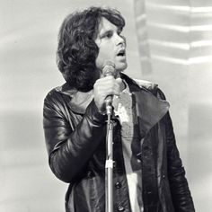 a man holding a microphone in his right hand and wearing a leather jacket on top of it